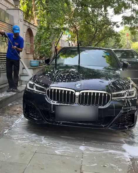 A freshly washed black BMW with a washer rinsing the steps beside it