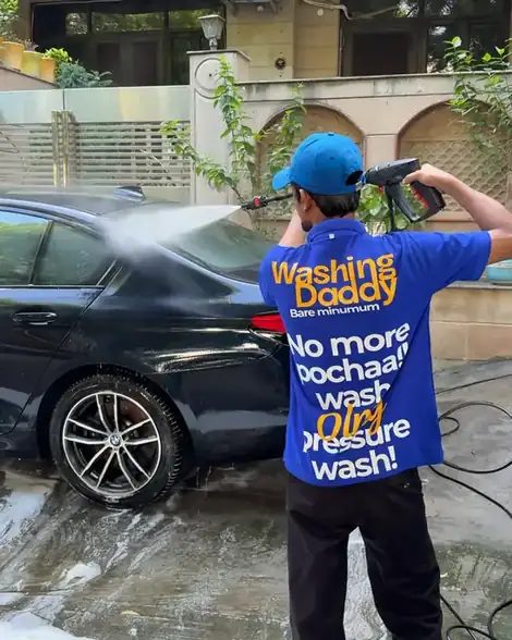 A Washing Daddy washer pressure-washing a black BMW, the back of his shirt reads No more pochaa, wash only pressure wash