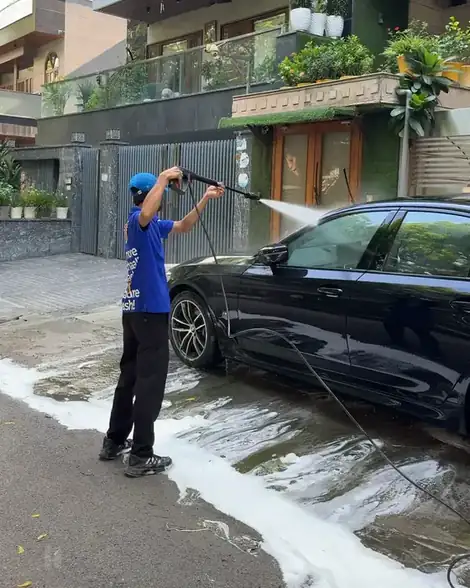 Washer pressure-rinsing a black sedan outside a house