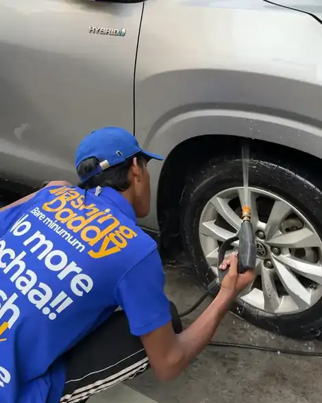 Washer crouching to pressure-wash the wheel of a silver Toyota hybrid